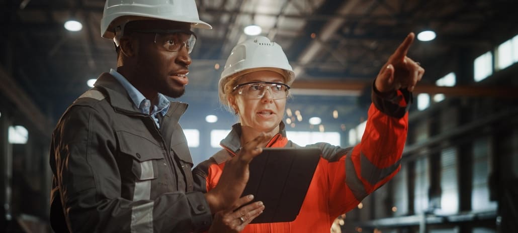 Two Heavy Industry Engineers Stand in Steel Metal Manufacturing Factory, Use Digital Tablet Computer and Have a Discussion.